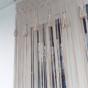Puede incluir: Un tapiz de macram&eacute; blanco con un patr&oacute;n geom&eacute;trico y borlas. El tapiz est&aacute; hecho de cord&oacute;n de algod&oacute;n natural y est&aacute; colgado de una varilla blanca.