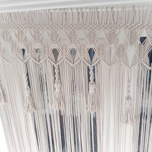 Puede incluir: Un tapiz de macram&eacute; blanco con un patr&oacute;n de diamante y borlas.