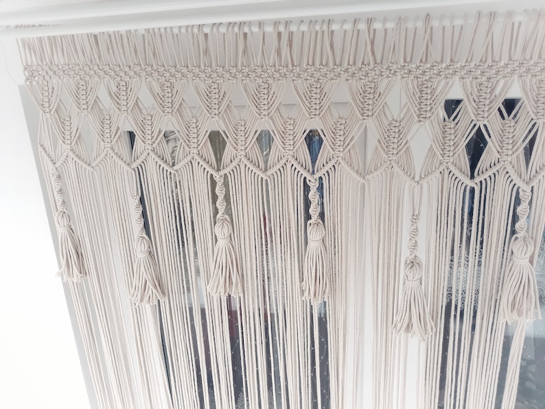 Puede incluir: Un tapiz de macram&eacute; blanco con un patr&oacute;n de diamante y borlas.