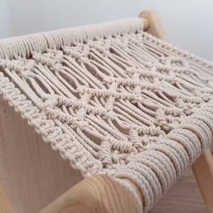 Op de afbeelding: Een macram&eacute; kruk met een zitting van natuurlijke beige touw en houten poten. De zitting is geweven in een ruitpatroon.