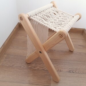Op de afbeelding: Een houten kruk met een macram&eacute; zitting. De kruk is gemaakt van natuurlijk hout en heeft een eenvoudig, rustiek ontwerp.