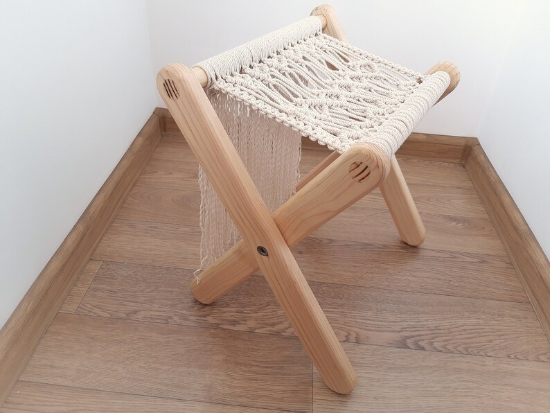 Op de afbeelding: Een houten kruk met een macram&eacute; zitting. De kruk is gemaakt van natuurlijk hout en heeft een eenvoudig, rustiek ontwerp.