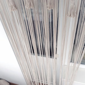 Puede incluir: Una cortina de macram&eacute; blanca con borlas que cuelgan en una puerta. La cortina est&aacute; hecha de muchos hilos de hilo que est&aacute;n anudados juntos.