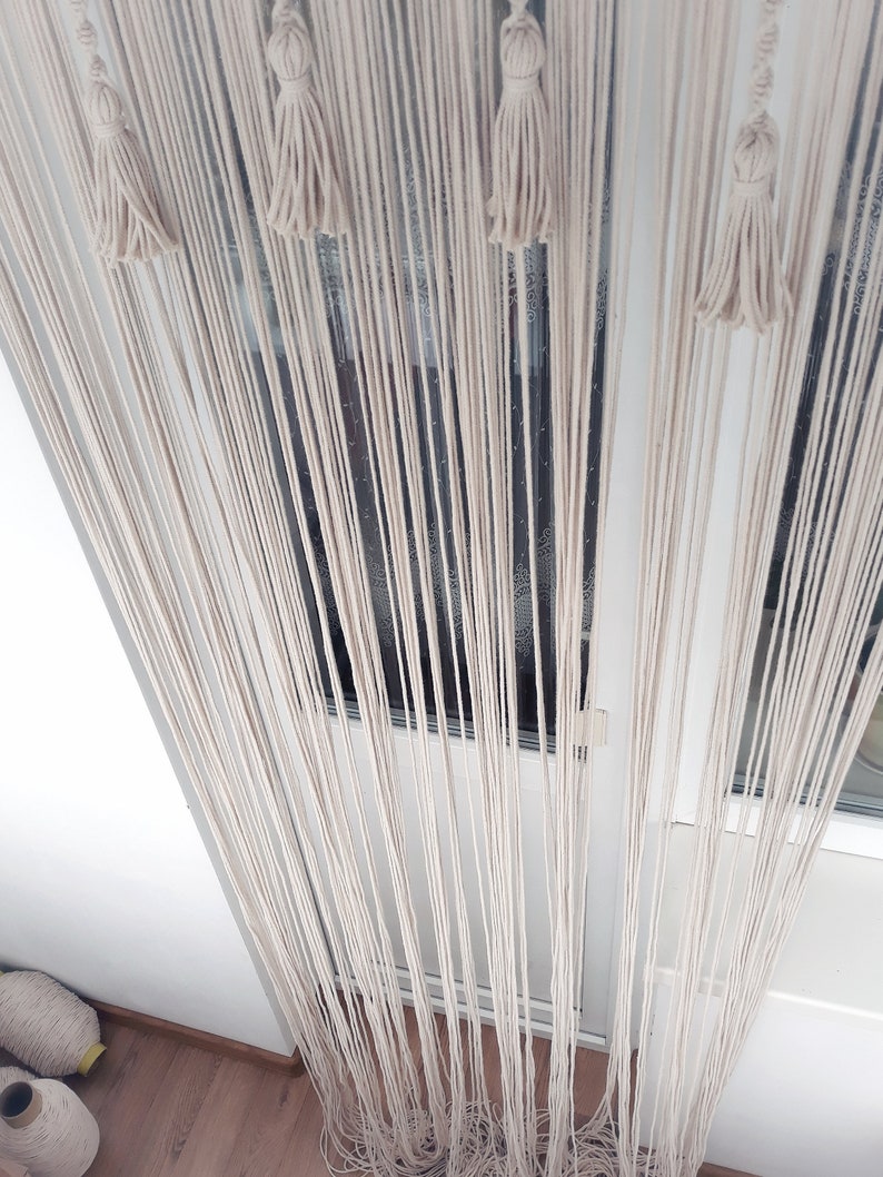 Puede incluir: Una cortina de macram&eacute; blanca con borlas que cuelgan en una puerta. La cortina est&aacute; hecha de muchos hilos de hilo que est&aacute;n anudados juntos.