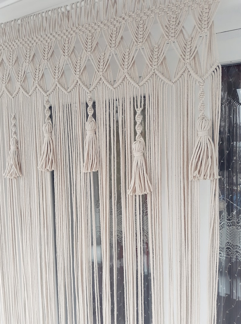 Puede incluir: Un tapiz de macram&eacute; blanco con un patr&oacute;n de diamante y borlas. El tapiz est&aacute; hecho de cord&oacute;n de algod&oacute;n y es un elemento de decoraci&oacute;n bohemia popular.