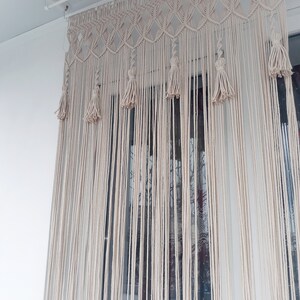Puede incluir: Una cortina de macram&eacute; blanca con borlas cuelga de una barra de techo blanca. La cortina est&aacute; hecha de cord&oacute;n de algod&oacute;n grueso y tiene un patr&oacute;n geom&eacute;trico.