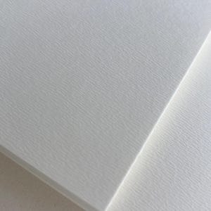 Peut inclure: Gros plan sur deux feuilles de papier blanc texturé. Le papier présente un motif subtil et strié, créant une surface tactile. Les feuilles sont inclinées, l'une chevauchant partiellement l'autre, mettant en valeur la texture et la couleur du papier.