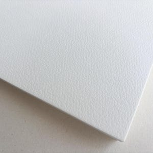 May include: Close-up of a white, textured surface with a slightly rough, pebbled appearance. The surface is angled, revealing a clean edge and a contrasting, smooth white background. The texture suggests a durable material.