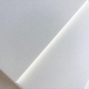May include: Close-up of two white textured paper sheets. The sheets are angled, with one overlapping the other. The paper has a subtle, granular texture, and the lighting creates soft shadows.