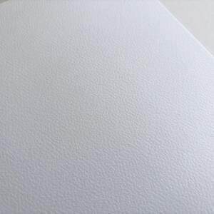 May include: Close-up of a textured white surface. The surface has a subtle, irregular pattern, creating a slightly rough appearance. The image is well-lit, highlighting the texture and the clean, neutral color.