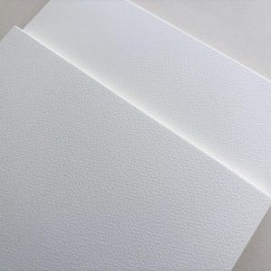 May include: Close-up of several white textured paper sheets, slightly overlapping. The paper has a subtle, speckled pattern, and the lighting creates soft shadows. The overall effect is clean and minimalist, suggesting a focus on texture and surface.