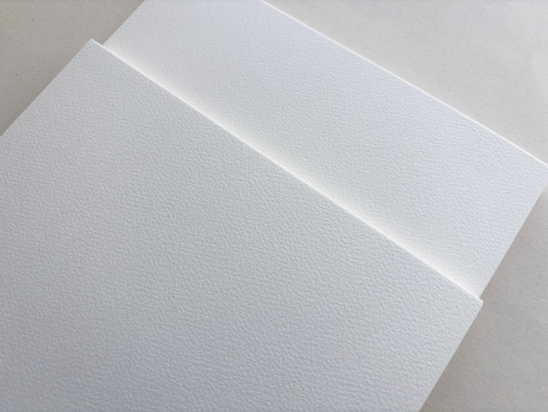 May include: Close-up of several white textured paper sheets, slightly overlapping. The paper has a subtle, speckled pattern, and the lighting creates soft shadows. The overall effect is clean and minimalist, suggesting a focus on texture and surface.