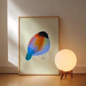 May include: A rectangular framed print featuring a stylised, round bird illustration with a black head and a vibrant, multi-coloured body in shades of orange, blue, and purple, set against a pale, neutral-toned background within a light wood frame.