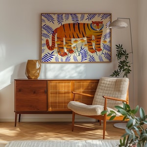 Puede incluir: Una l&aacute;mina art&iacute;stica enmarcada que muestra un tigre naranja con rayas negras entre flores amarillas y hojas de helecho azules. La obra se exhibe sobre un aparador de madera con puertas de rejilla, un jarr&oacute;n dorado facetado y un sill&oacute;n color crema.