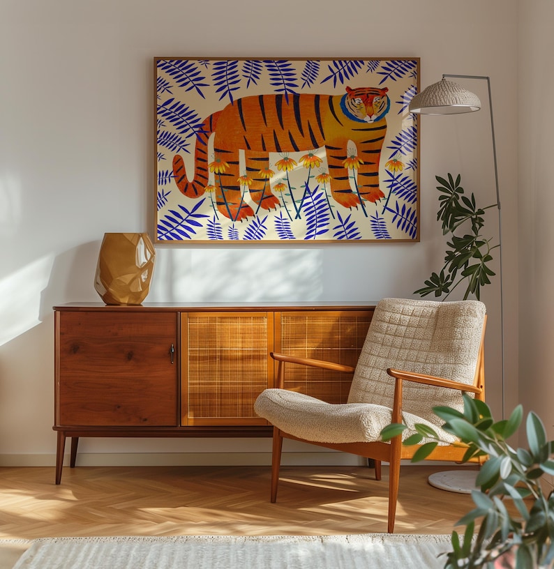 Puede incluir: Una l&aacute;mina art&iacute;stica enmarcada que muestra un tigre naranja con rayas negras entre flores amarillas y hojas de helecho azules. La obra se exhibe sobre un aparador de madera con puertas de rejilla, un jarr&oacute;n dorado facetado y un sill&oacute;n color crema.