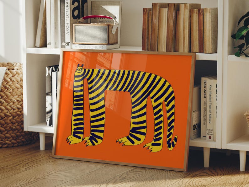 May include: A framed rectangular wall art print featuring a stylized illustration of a long-bodied, four-legged creature with yellow and black stripes on a solid orange background. The creature has a small head, elongated neck, and paws.
