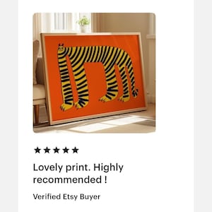 May include: A rectangular framed wall art print featuring a stylized, long-bodied creature with black vertical stripes on a vibrant orange background. The creature has four legs, a small head with ears, and a tail, all rendered in a bold, graphic style.