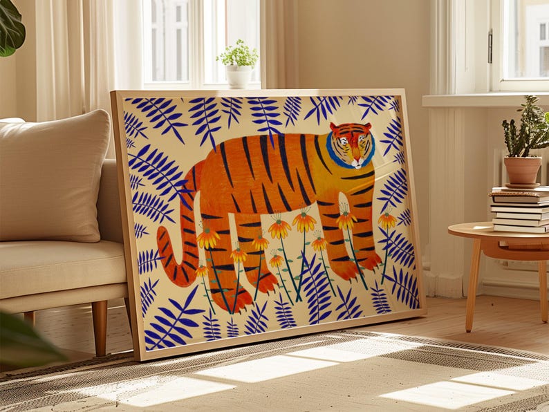 May include: A framed rectangular wall art print featuring a large orange tiger with black stripes standing amidst a pattern of blue fern-like leaves and yellow flowers on a cream-coloured background, enclosed in a light-toned wooden frame.