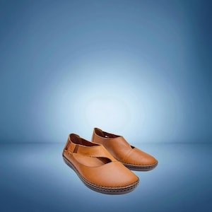 May include: A pair of tan leather flats with a rounded toe and a strap across the top. The shoes have a stitched sole and are set against a blue gradient background.