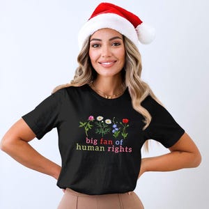 May include: A black t-shirt with a floral design and the text "big fan of human rights" in colorful letters. The person in the image is wearing a red and white Santa hat.