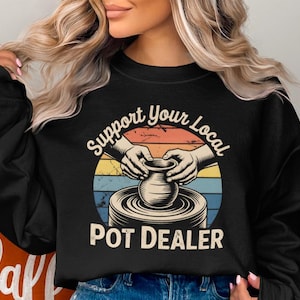 May include: Black sweatshirt with a circular graphic featuring hands shaping a pot on a pottery wheel. The graphic has a retro color scheme with the text "Support Your Local Pot Dealer".
