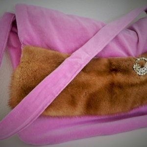 May include: A pink velvet handbag with a brown fur flap and a rhinestone brooch. The bag has a long strap.