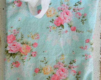 Puede incluir: Una bolsa de tela azul claro con asas blancas y un estampado floral con rosas rosas y amarillas.