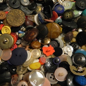 Peut inclure: Un assortiment de boutons de différentes tailles, formes et couleurs. Les boutons comprennent du noir, du blanc, du jaune, du rouge et du marron, certains ayant des textures et des motifs uniques. Fabriqués en plastique, métal et tissu.