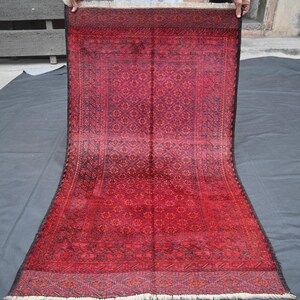 May include: A rectangular, red rug with a detailed geometric pattern. The rug has a dark border and a lighter red centre, with a fringe on one end. The design features repeating floral and star-like motifs.