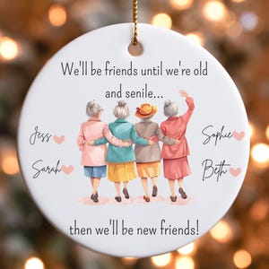 May include: A white ceramic ornament with a gold string for hanging. The ornament features an illustration of four elderly women arm-in-arm. Text reads "We'll be friends until we're old and senile... then we'll be new friends!" Names Jess, Sarah, Sophie, and Beth are also included.