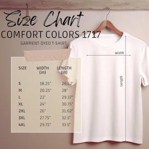K&ouml;nnte beinhalten: Ein wei&szlig;es Comfort Colors 1717-T-Shirt, das an einem Holzb&uuml;gel h&auml;ngt. Eine Gr&ouml;&szlig;entabelle zeigt die Ma&szlig;e in Zoll f&uuml;r die Gr&ouml;&szlig;en S bis 4XL, einschlie&szlig;lich Breite und L&auml;nge.