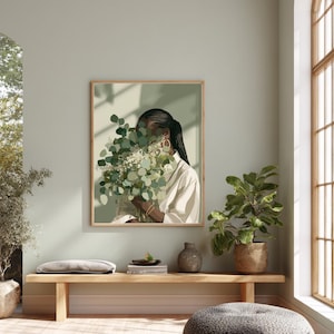 May include: A framed art print featuring a person holding a bouquet of green and white flowers. The person is wearing a white shirt and gold hoop earrings. The artwork is displayed in a room with a wooden bench and potted plants.