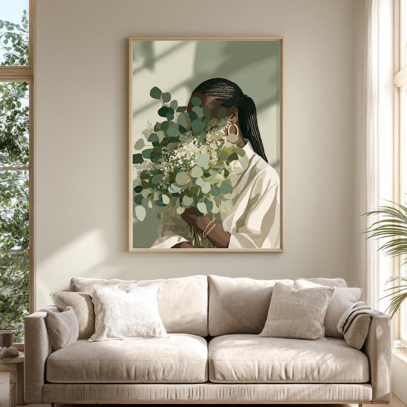 May include: A framed art print featuring a person holding a bouquet of green and white flowers, with a light green background. The person is wearing a white shirt and gold hoop earrings. The artwork is displayed above a beige sofa.