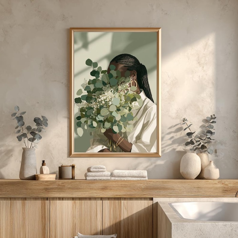 May include: A framed art print featuring a person holding a bouquet of green and white flowers. The person is wearing a white shirt and gold hoop earrings. The artwork has a neutral color palette and is displayed in a bathroom setting.