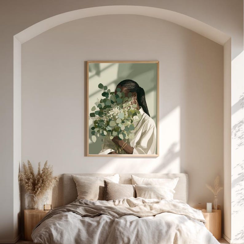 May include: A framed art print depicts a person holding a bouquet of green and white flowers, with the face partially obscured. The person is wearing a white shirt and gold hoop earrings. The artwork is displayed above a bed with neutral-toned bedding.