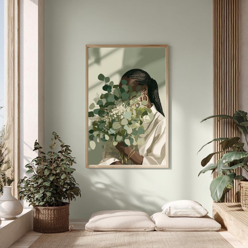 May include: A framed art print featuring a person holding a bouquet of green and white flowers, with a light green background. The person is wearing a white shirt and gold hoop earrings. The artwork is displayed in a well-lit room with plants.