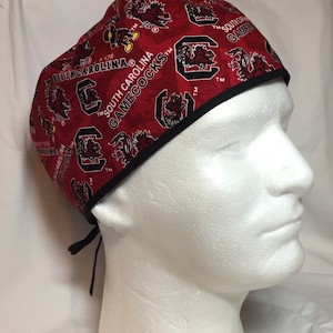 May include: Red and black surgical scrub hat with a repeating pattern of the University of South Carolina Gamecocks logo and the words "South Carolina Gamecocks".