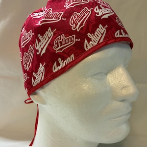 May include: Red and white patterned cap featuring the word "Indiana" repeated across the fabric. The cap has a red trim and ties at the back. The cap is displayed on a white mannequin head.