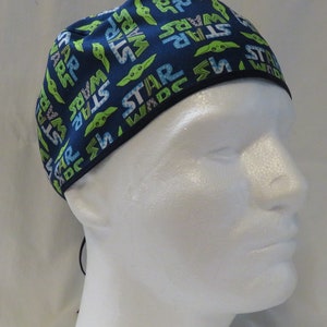 May include: A blue and green patterned scrub hat with the words "STAR WARS" repeated throughout. The hat has a black drawstring.
