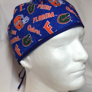 May include: Blue scrub cap with an all-over pattern featuring orange football helmets, the word "Gators", and the word "Florida". The cap has a blue trim and ties in the back.