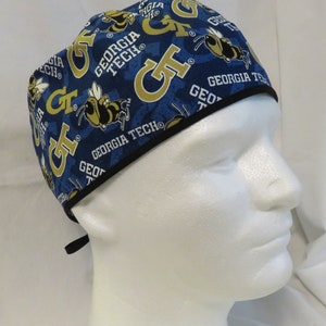May include: A blue and gold surgical scrub hat with a repeating pattern of the Georgia Tech logo and a bee. The hat has a black elastic band.