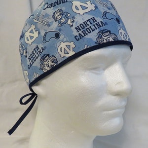 May include: Blue and white patterned surgical scrub hat with a navy blue trim. The hat features the text "Tar Heels", "Carolina", "North Carolina", and "UNC" along with a blue footprint and a cartoon ram.