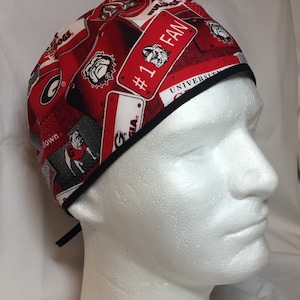 May include: Red and white surgical scrub hat with a black trim. The hat features a repeated pattern of license plates with the words "#1 Fan", "Georgia", and "Bulldogs".