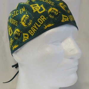 May include: Green and gold surgical scrub hat with a Baylor University logo and the words "Sic 'Em Bears" repeated on the fabric.