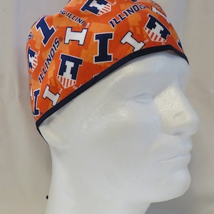 May include: Orange and blue patterned scrub cap featuring the word "ILLINOIS" and the letter "I" with a shield design. The cap has a navy blue trim and is tied in the back.