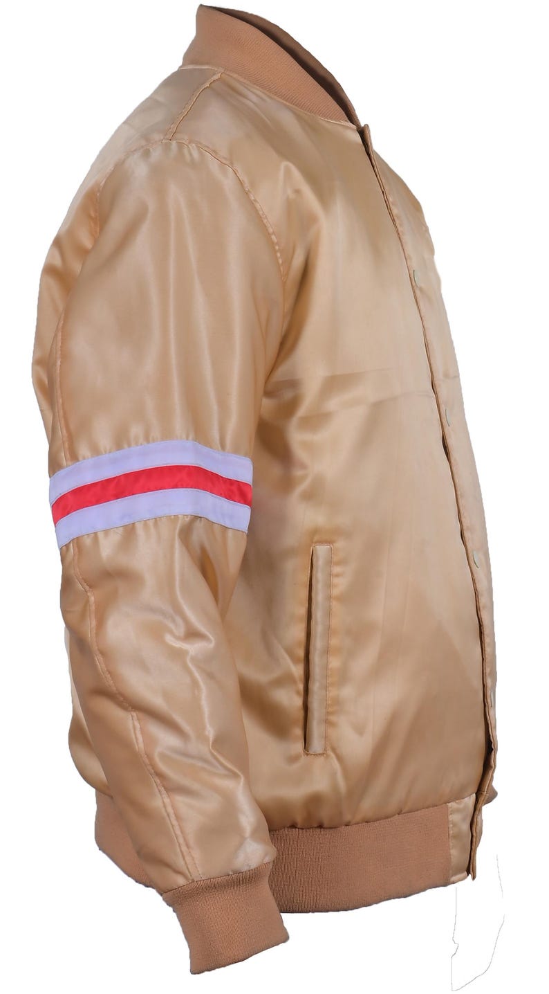 May include: A tan satin bomber jacket with a ribbed collar, cuffs, and waistband. The left sleeve features a white and red striped detail. The jacket has a button-up front and a single pocket.