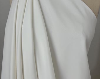 May include: A draped, off-white fabric is displayed on a mannequin. The fabric is folded and gathered, creating soft, flowing lines. The material appears to be smooth and opaque, with a subtle sheen. The overall impression is of elegance and simplicity.