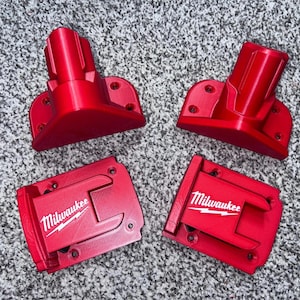 May include: Four bright red power tool accessories. Two have a cylindrical shape, and two have a rectangular shape with the "Milwaukee" logo in white. The items are made of a hard plastic material.