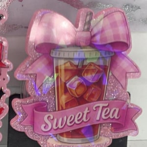 May include: A pink glitter badge reel featuring a sweet tea design. The design includes a cup of iced tea with ice cubes, a pink bow, and a banner that reads "Sweet Tea". The badge reel has a clear plastic retractable cord.