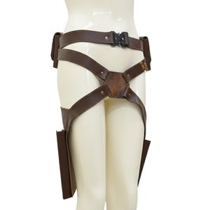 May include: Brown leather utility belt with two pouches and leg straps. The belt features a black buckle and is designed to be worn around the waist and thighs. The leather has a slightly distressed appearance.